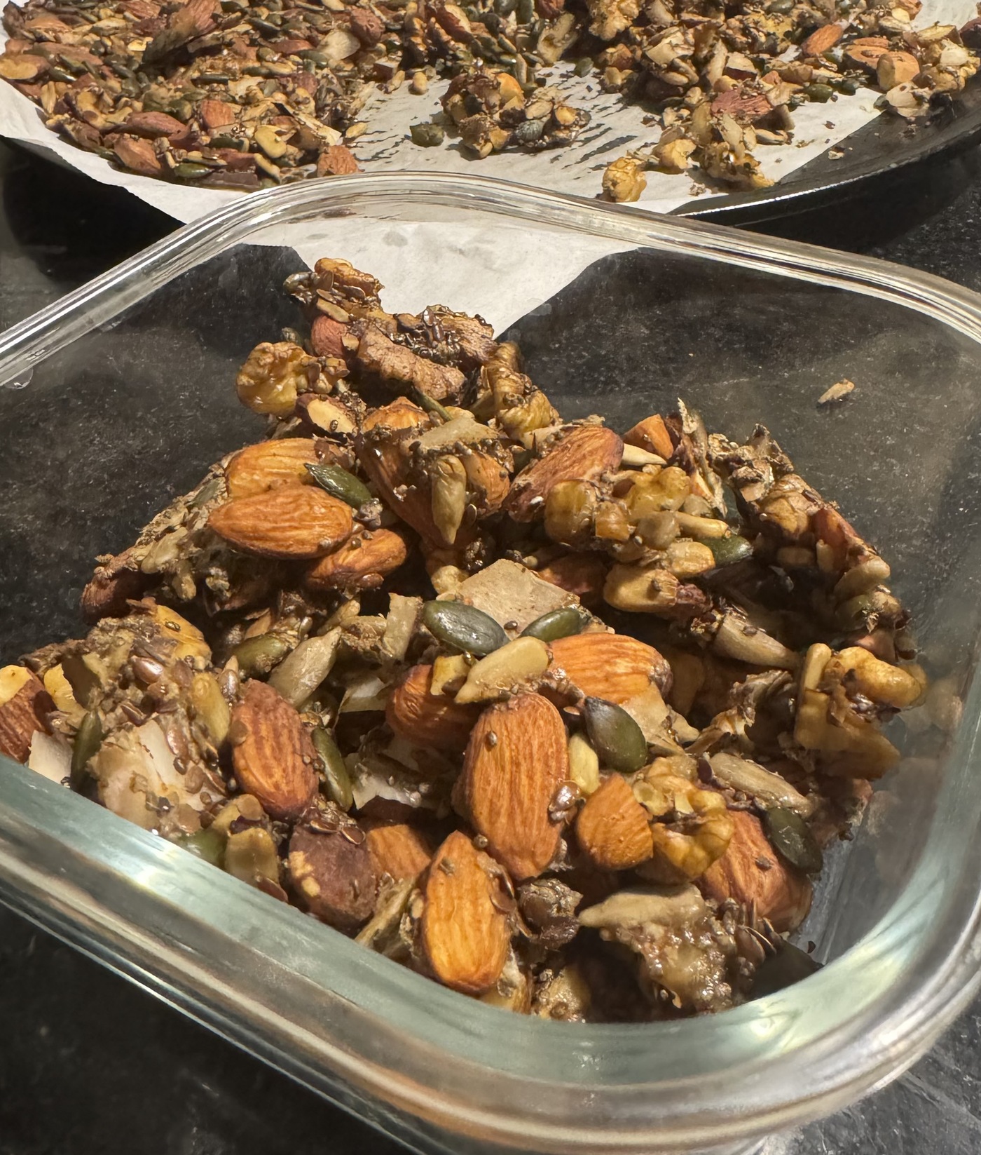 Egg-free keto granola clusters broken up on the baking tray, with a container of finished clusters in front