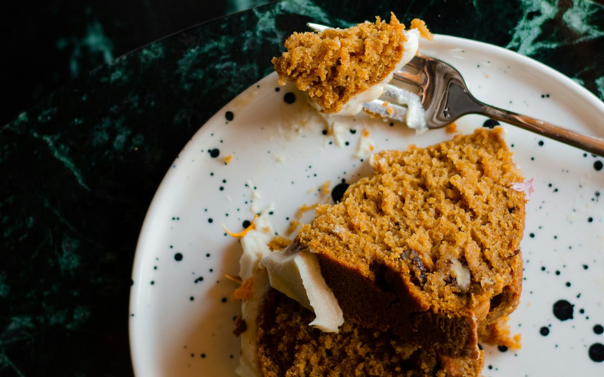 A slice of spiced pumpkin cake with cream cheese on a speckled plate
