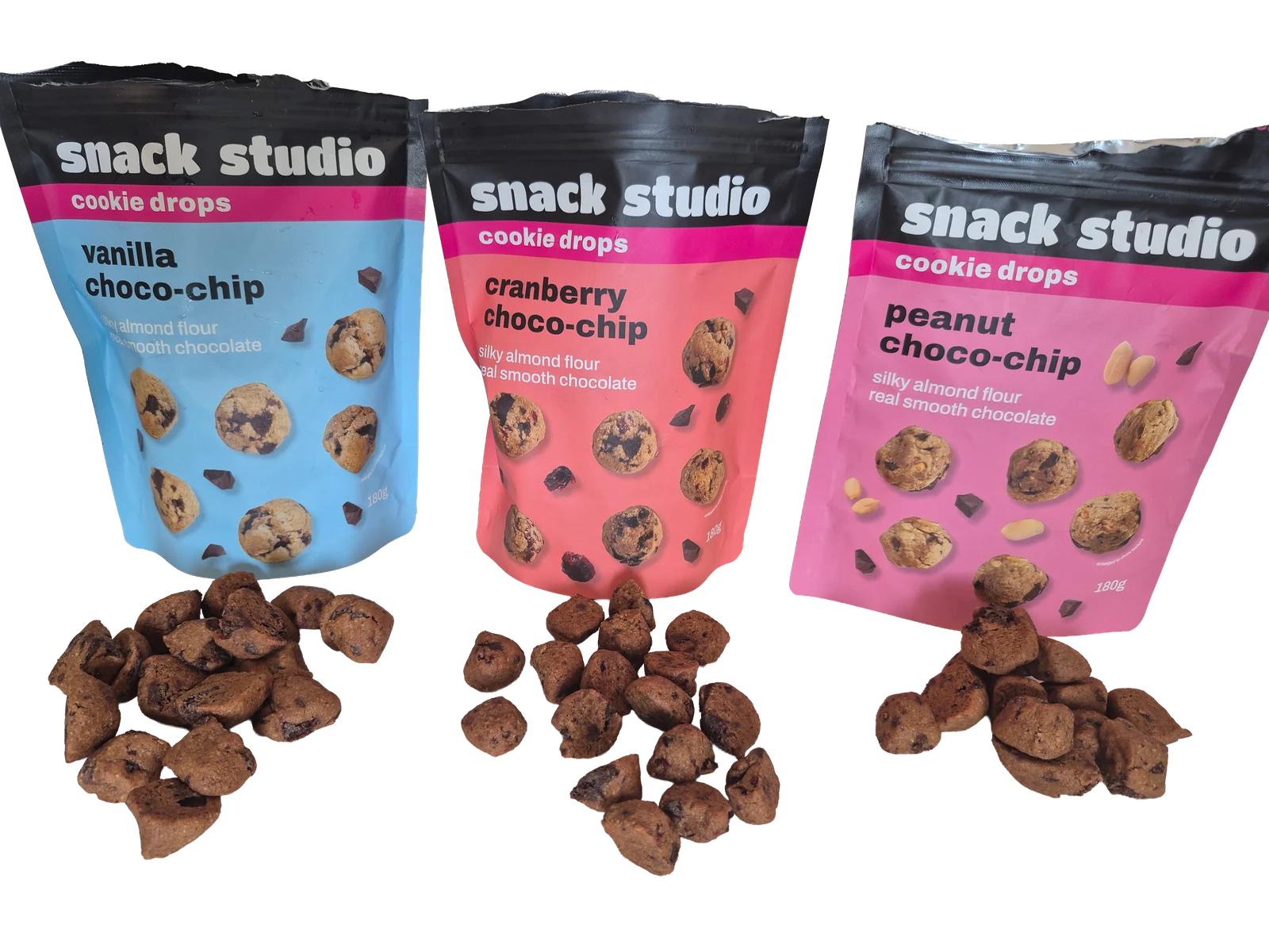 Three Snack Studio cookie drops packets, vanilla, cranberry and peanut choco-chip, with cookie drops scattered in front of each